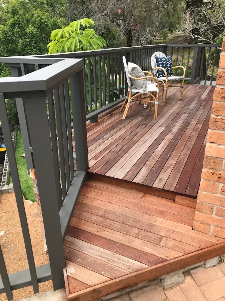 Timber deck and step framed by grey painted balustrades beside a brick home