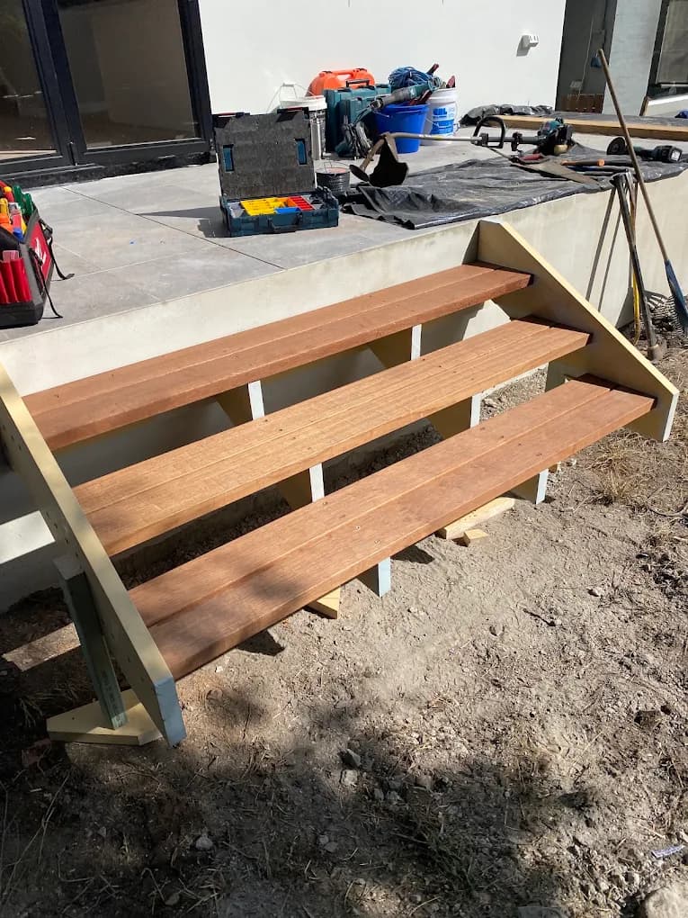 Wide timber steps with open risers leading to a patio, with tools visible during construction