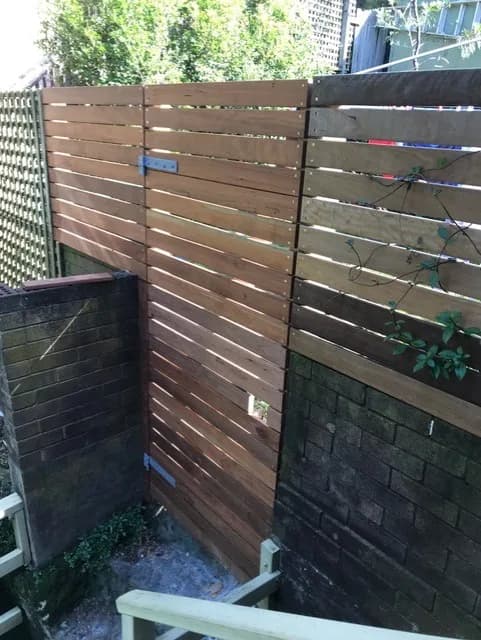 Horizontal timber slat fence panels and a gate above a rendered block wall